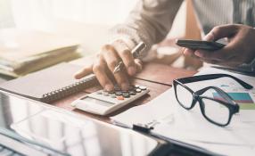 Image of a person at a table at a laptop, and using a calculator and pen