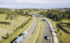 This is an image of a truck going down a highway with green fields on both sides