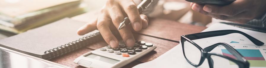 Image of a person at a table at a laptop, and using a calculator and pen