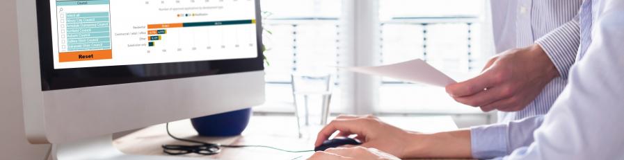 Image of a person leaning over another pointing at a computer and holding a document